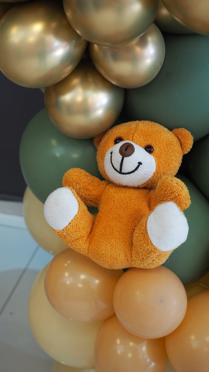Charming orange teddy bear nestled in a vibrant balloon arrangement indoors.